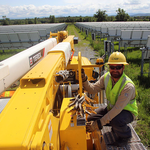 Lineworker on bucket truck with Panton solar field behind him in summertime on sunny, partly cloudy day.