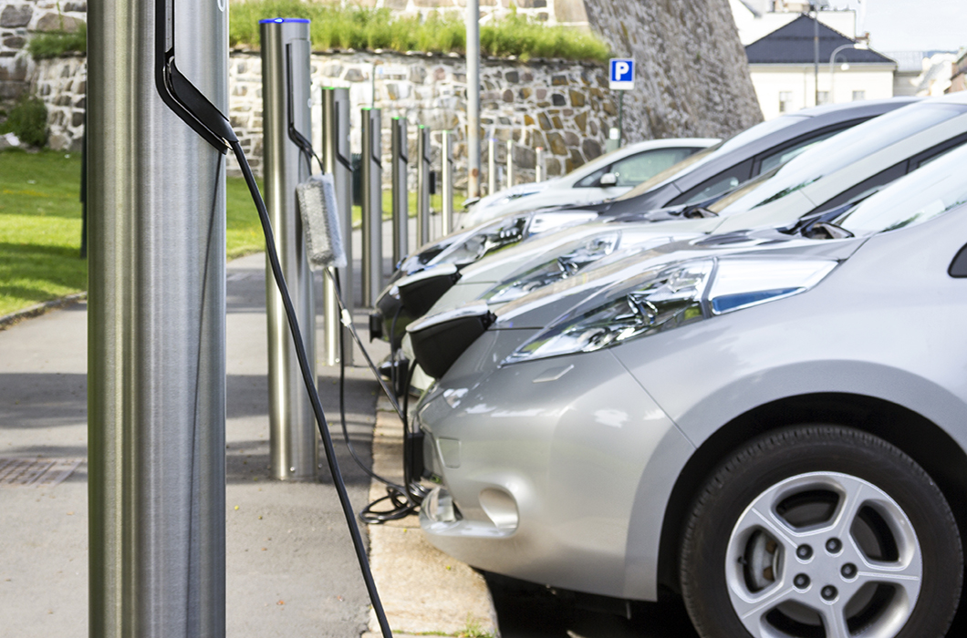 Fleet of vehicles lined up at multiple charging stations on summer day.